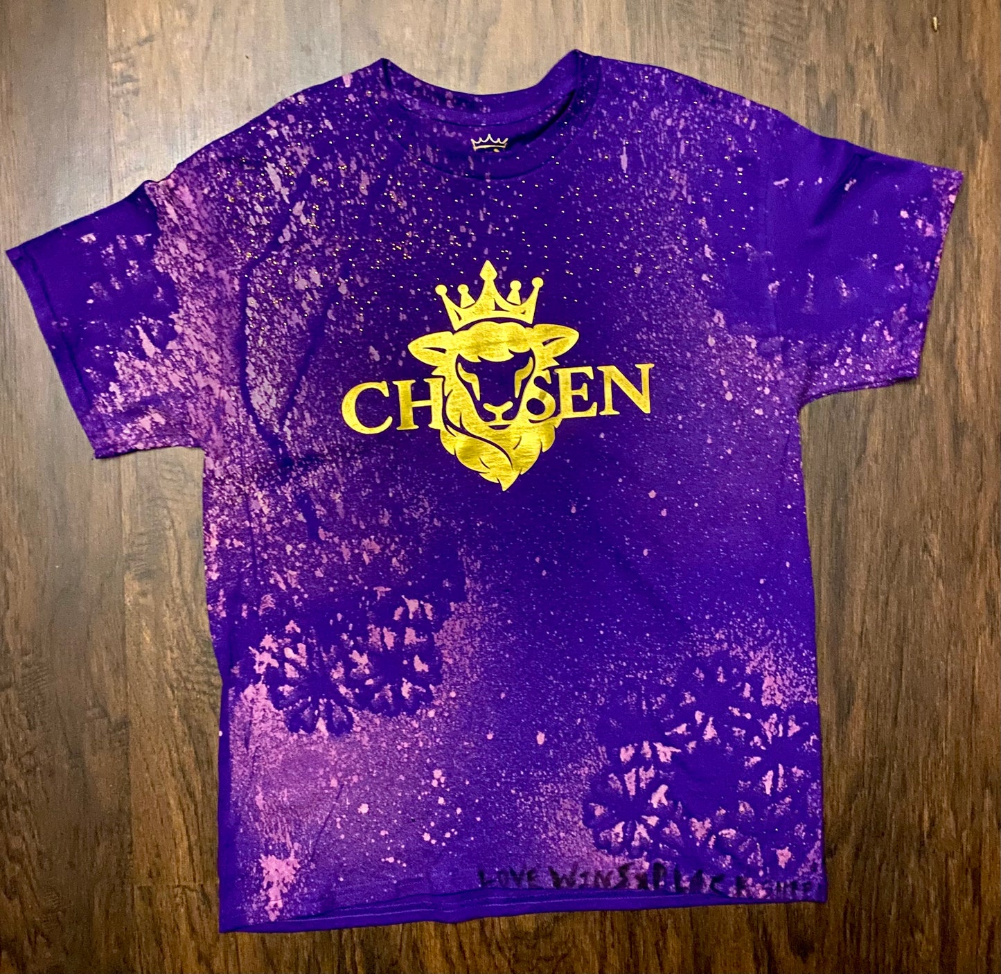 Purple t-shirt with yellow graphic and text on a wooden surface