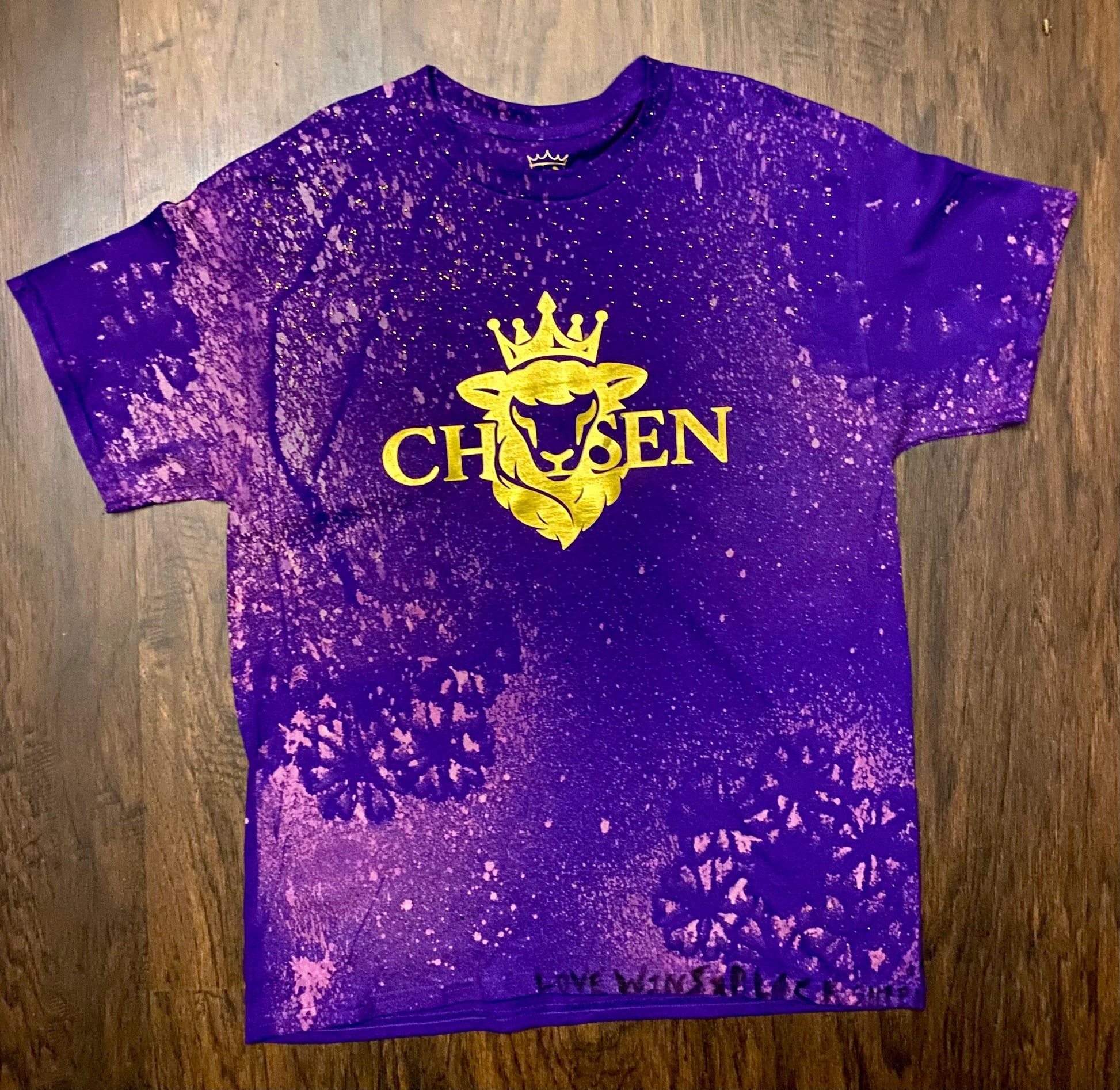 Purple t-shirt with yellow graphic and text on a wooden surface