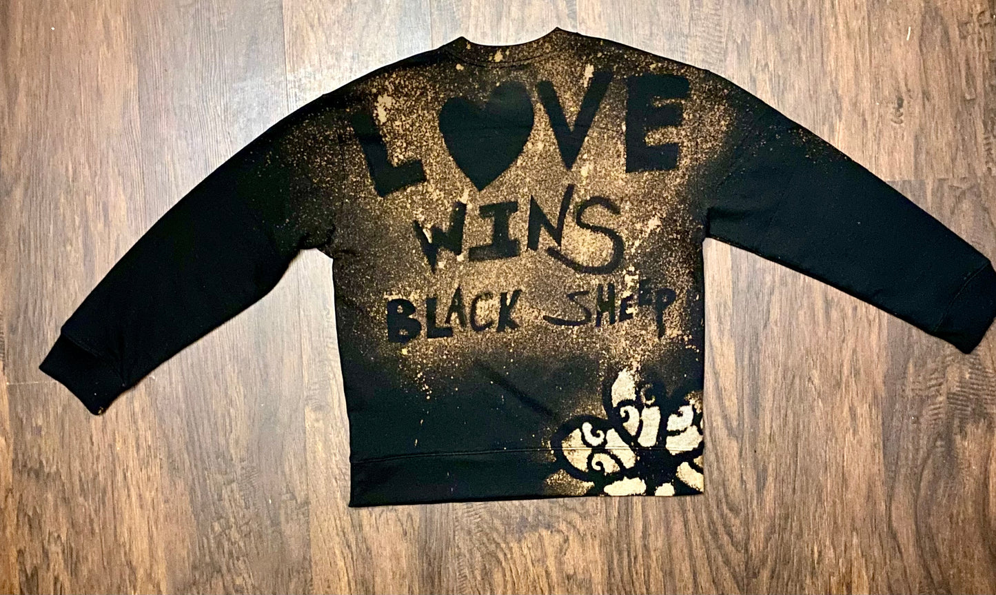 Black sweatshirt with 'Love Wins' text on a wooden surface