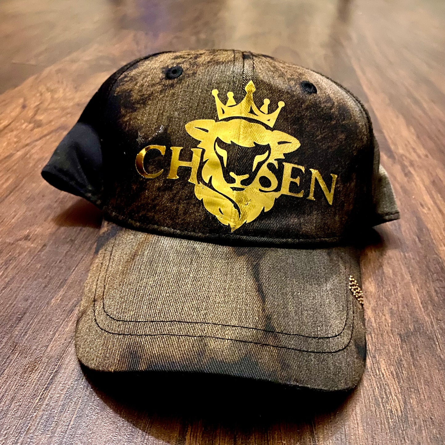 Brown cap with gold logo and text on a wooden surface